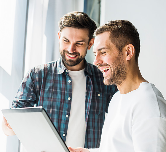 Two men smiling white looking at a laptop screen