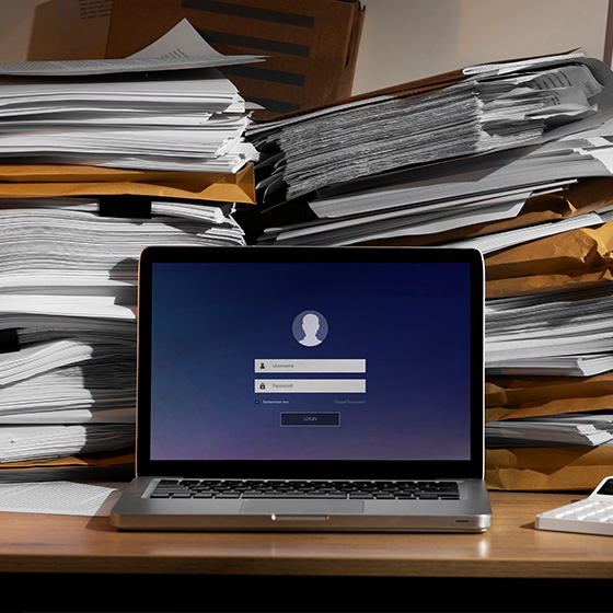 A laptop and stacks of paper on a table